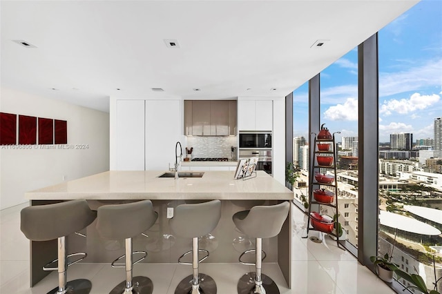 kitchen featuring backsplash, white cabinets, a kitchen breakfast bar, sink, and black microwave