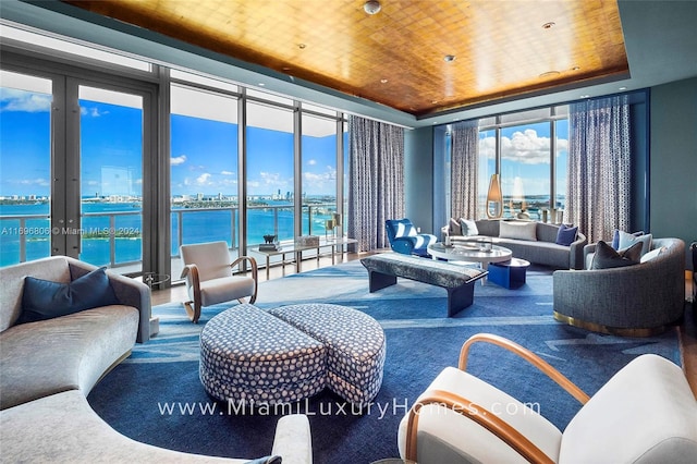 carpeted living room with a raised ceiling, a water view, and wood ceiling