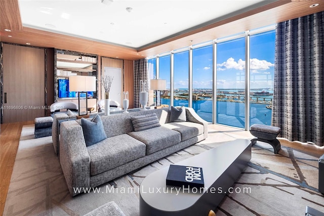 living room with hardwood / wood-style floors, a water view, a wall of windows, and wood walls