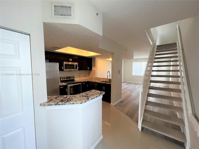 kitchen with light stone countertops, sink, stainless steel appliances, a textured ceiling, and light wood-type flooring