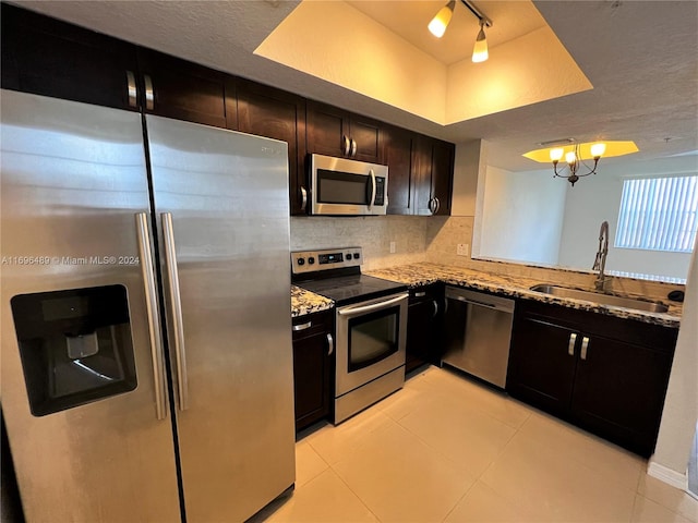 kitchen featuring appliances with stainless steel finishes, backsplash, light stone counters, sink, and a chandelier