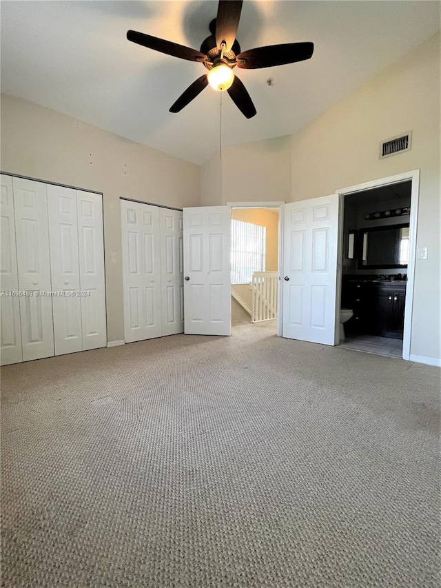 unfurnished bedroom featuring carpet flooring, ceiling fan, multiple closets, and ensuite bath