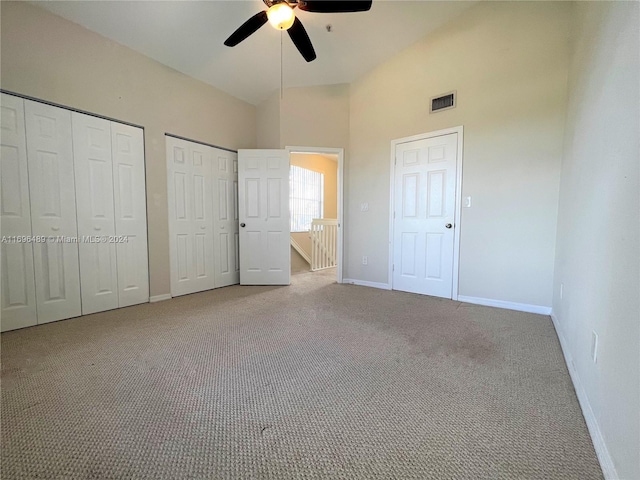 unfurnished bedroom with ceiling fan, high vaulted ceiling, light carpet, and two closets