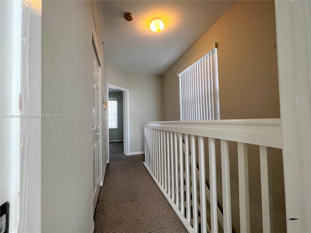 corridor featuring a textured ceiling and dark carpet