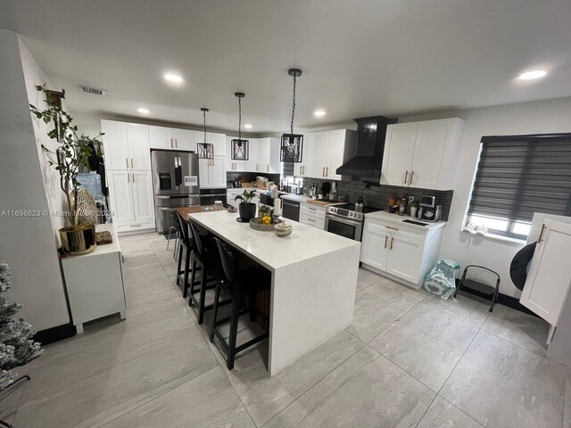 kitchen featuring pendant lighting, white cabinets, wall chimney range hood, a kitchen island, and stainless steel appliances