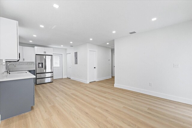 kitchen with sink, stainless steel fridge, decorative backsplash, white cabinets, and light wood-type flooring