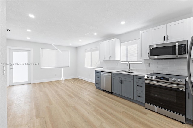 kitchen featuring gray cabinetry, sink, light wood-type flooring, appliances with stainless steel finishes, and white cabinetry