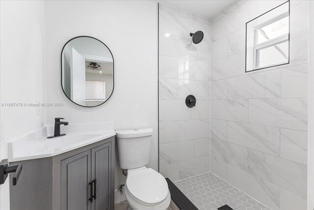 bathroom featuring a tile shower, vanity, and toilet