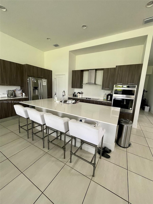 kitchen with visible vents, appliances with stainless steel finishes, wall chimney range hood, modern cabinets, and a kitchen bar