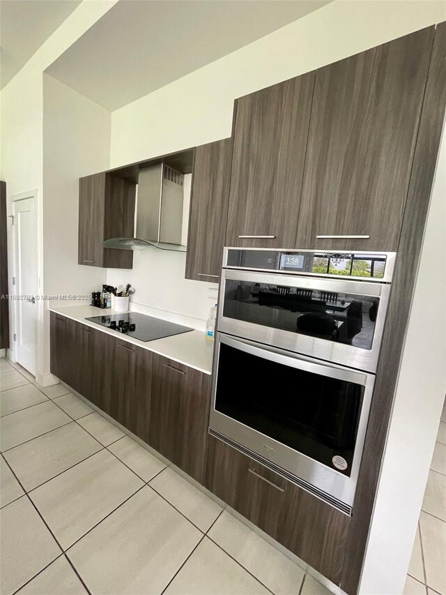 kitchen with wall chimney range hood, modern cabinets, black electric stovetop, and light tile patterned floors