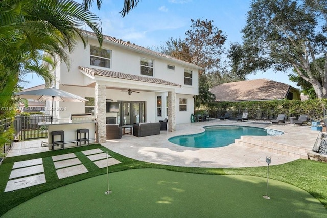 back of property featuring ceiling fan, an outdoor kitchen, a fenced in pool, a bar, and a patio