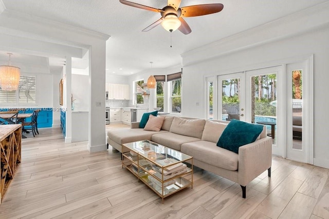 living room featuring french doors, ceiling fan with notable chandelier, light hardwood / wood-style flooring, and ornamental molding