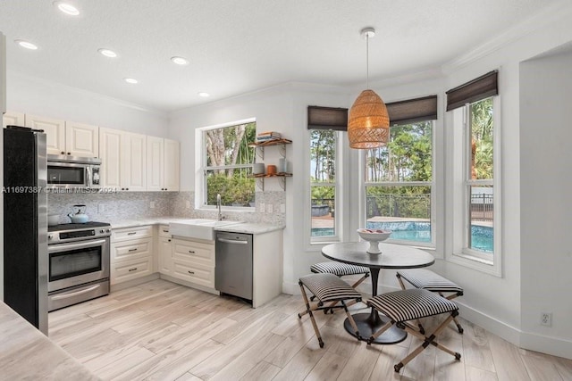 kitchen featuring pendant lighting, sink, decorative backsplash, light wood-type flooring, and appliances with stainless steel finishes