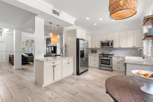 kitchen with decorative backsplash, appliances with stainless steel finishes, light wood-type flooring, ornamental molding, and white cabinetry