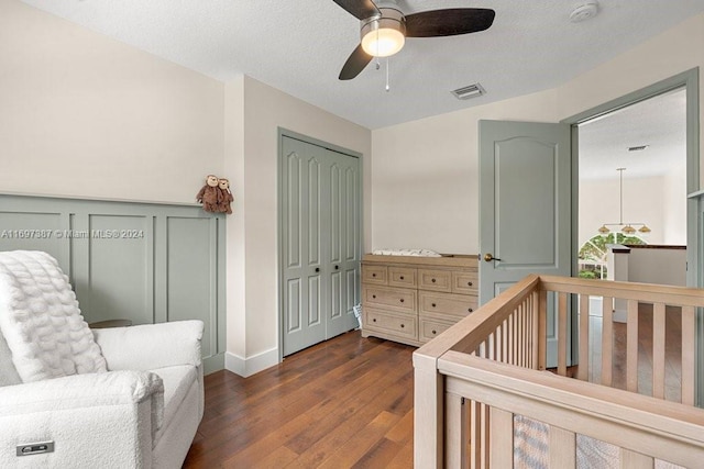 bedroom featuring ceiling fan, dark hardwood / wood-style floors, a textured ceiling, a closet, and a crib