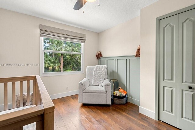 bedroom with a textured ceiling, ceiling fan, a nursery area, hardwood / wood-style floors, and a closet