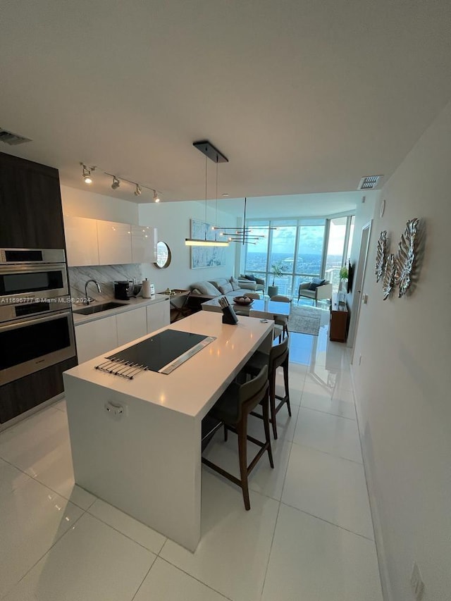 kitchen featuring white cabinets, hanging light fixtures, black stovetop, light tile patterned floors, and a kitchen island