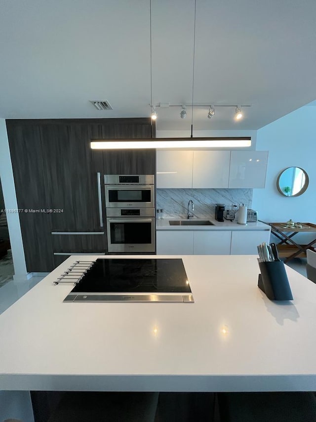 kitchen with sink, cooktop, backsplash, double oven, and white cabinets