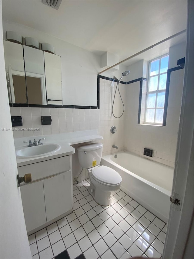 full bathroom featuring tile patterned floors, vanity, tiled shower / bath combo, tile walls, and toilet