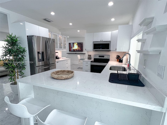 kitchen with white cabinets, light stone counters, appliances with stainless steel finishes, a kitchen bar, and kitchen peninsula