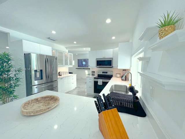 kitchen with light stone counters, stainless steel appliances, white cabinetry, and sink