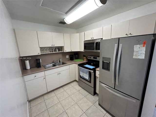 kitchen with sink, light tile patterned floors, a textured ceiling, appliances with stainless steel finishes, and white cabinetry