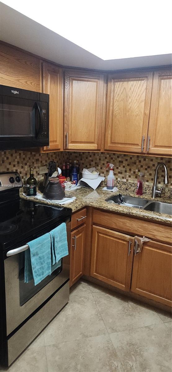 1201 S Ocean Dr Unit 304S, Hollywood, FL 33019 - kitchen featuring stainless steel electric range oven, black microwave, backsplash, brown cabinets, and light tile patterned floors