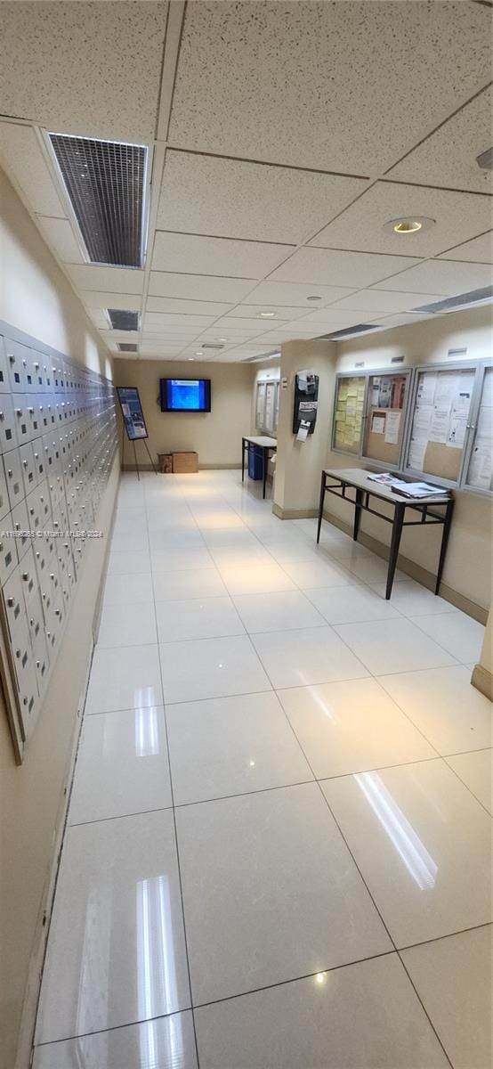 hallway featuring tile patterned flooring, a drop ceiling, and a mail area