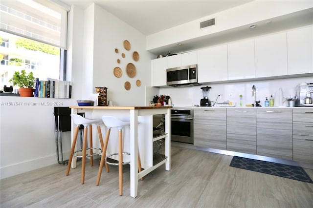 kitchen with appliances with stainless steel finishes, light wood-type flooring, a kitchen breakfast bar, sink, and white cabinetry