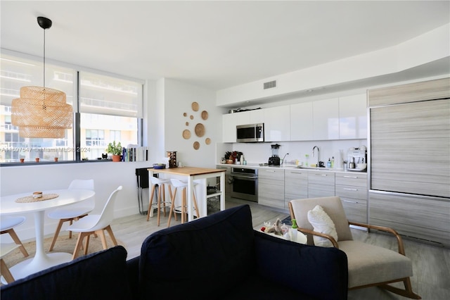 kitchen featuring sink, stainless steel appliances, light hardwood / wood-style flooring, decorative light fixtures, and white cabinets