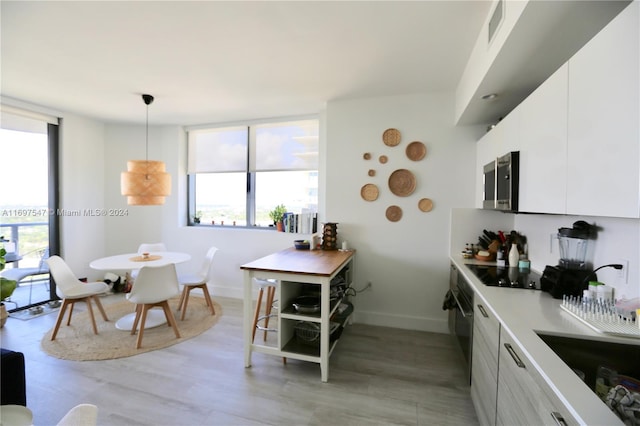 kitchen with sink, pendant lighting, light hardwood / wood-style floors, white cabinets, and black appliances