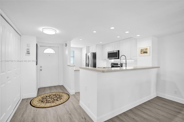 kitchen with sink, stainless steel appliances, kitchen peninsula, white cabinets, and light wood-type flooring