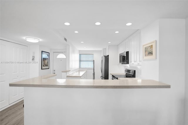 kitchen with light hardwood / wood-style floors, white cabinetry, kitchen peninsula, and appliances with stainless steel finishes