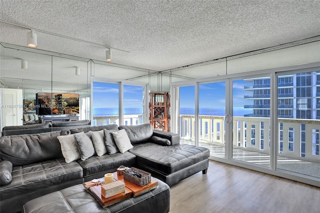 living room with floor to ceiling windows, a textured ceiling, a water view, and hardwood / wood-style flooring