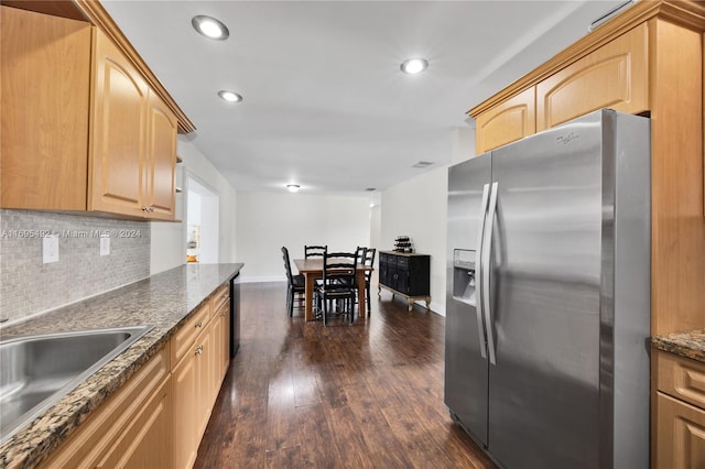 kitchen with light brown cabinets, dark wood-type flooring, backsplash, dark stone countertops, and stainless steel fridge