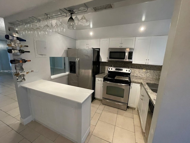 kitchen with light tile patterned floors, tasteful backsplash, kitchen peninsula, white cabinets, and appliances with stainless steel finishes