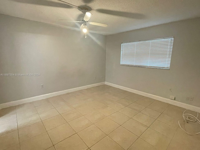 empty room with ceiling fan, light tile patterned flooring, and a textured ceiling