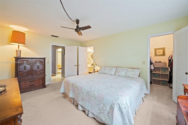 carpeted bedroom featuring ceiling fan, a spacious closet, and ensuite bath