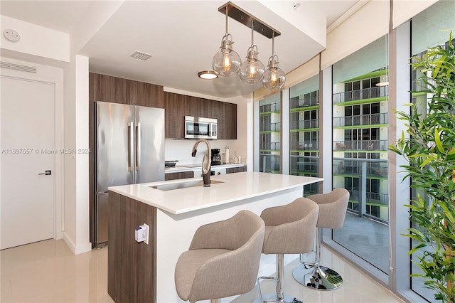 kitchen with appliances with stainless steel finishes, dark brown cabinetry, sink, pendant lighting, and a center island with sink