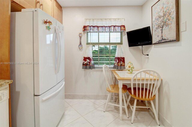 kitchen with light brown cabinetry, white fridge, and light tile patterned floors