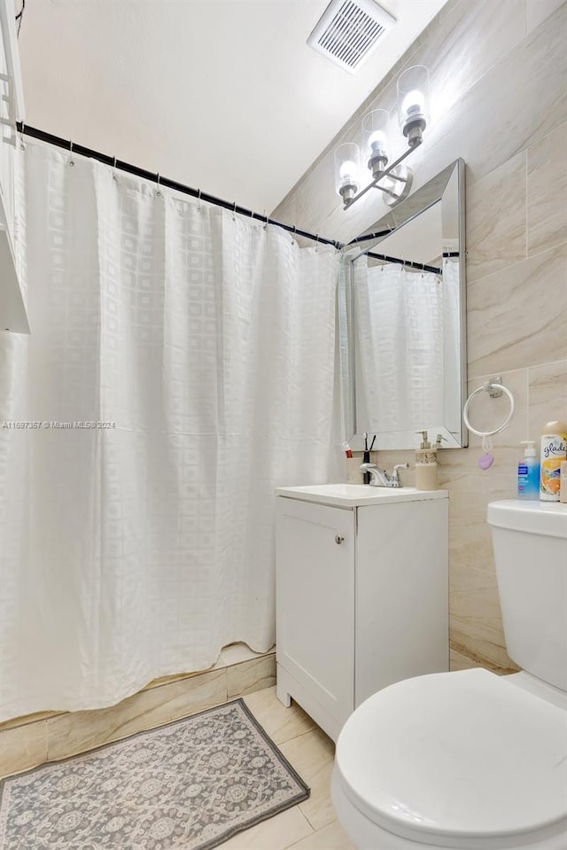 bathroom featuring curtained shower, tile patterned floors, toilet, vanity, and tile walls