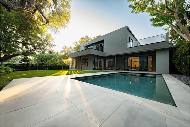 rear view of property featuring a balcony, a yard, stucco siding, an outdoor pool, and a patio area