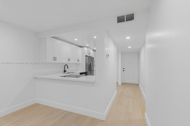 kitchen featuring sink, stainless steel refrigerator with ice dispenser, kitchen peninsula, light hardwood / wood-style floors, and white cabinets