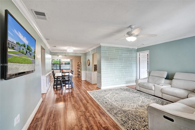 living room with ceiling fan, light hardwood / wood-style flooring, a textured ceiling, and ornamental molding