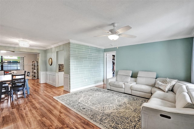 living room with a textured ceiling, light hardwood / wood-style flooring, ceiling fan, and ornamental molding