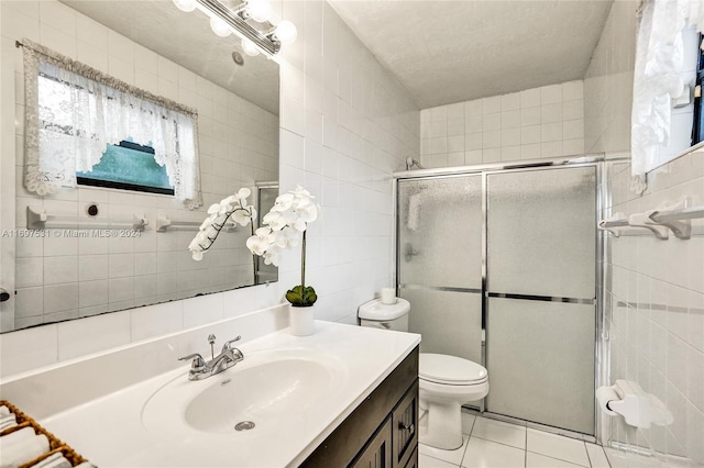 bathroom with tile patterned floors, vanity, a shower with door, tile walls, and toilet