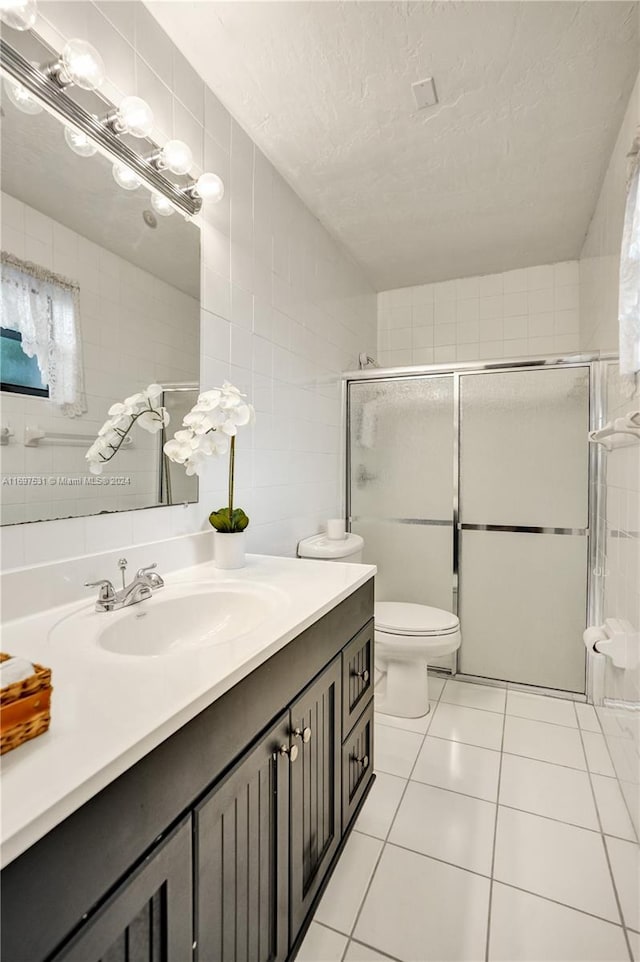 bathroom featuring tile patterned floors, vanity, tile walls, toilet, and a shower with shower door