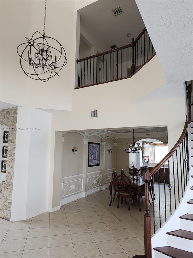 stairway with tile patterned flooring, a towering ceiling, a textured ceiling, and an inviting chandelier