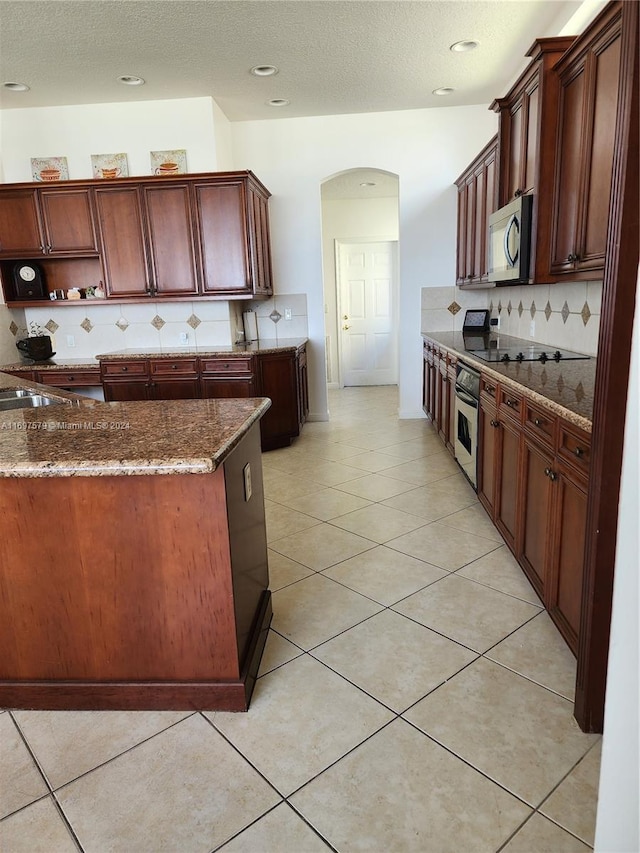 kitchen with stainless steel appliances, tasteful backsplash, dark stone counters, a textured ceiling, and light tile patterned floors