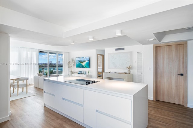 kitchen with light brown cabinets, a kitchen island, black electric stovetop, white cabinets, and hardwood / wood-style flooring